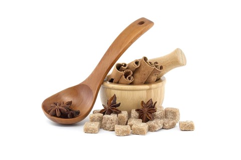 Star anise in a wooden spoon, wooden mortar filled with cinnamon sticks and brown sugar cubes