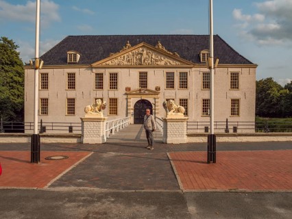 Man in front of a large historic manor house with lion statues and flagpoles in daylight, dornum,