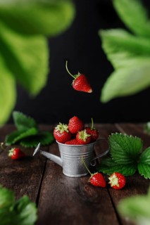 Fresh wet sweet strawberries levitation in watering can on wooden background table, black wall,
