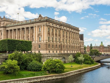 Impressive historic building on the canal with trees and bridge in the foreground under a partly