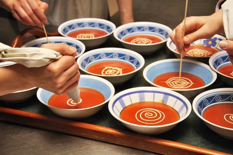 Busy cooks garnish bowls of tomato soup with fresh cream