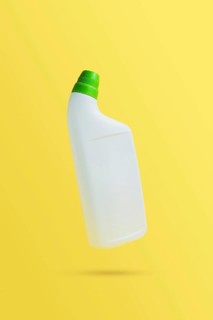 Levitating or flying blank toilet cleaner bottle with green cap. Isolated on yellow background.