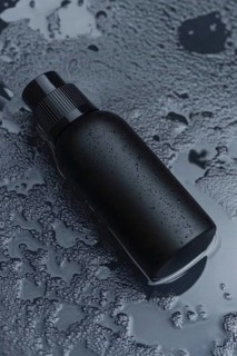 A sleek matte black bottle with water droplets on a dark, wet surface creating a minimalistic and