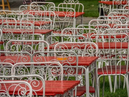 White-painted metal tables and chairs with red seats and table tops, standing in a pattern on a