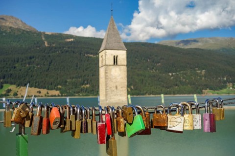 Bridge with countless padlocks, in the background a church tower and a mountain landscape with a