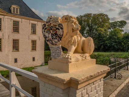 Lion statue with coat of arms on bridge wall, buildings and nature in the background, dornum, east