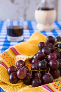 Closeup of a bunch of red grapes and a glass of red wine with a wine flask on background over a
