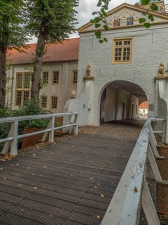 Wooden bridge and white archway in a historic building complex surrounded by autumn leaves and