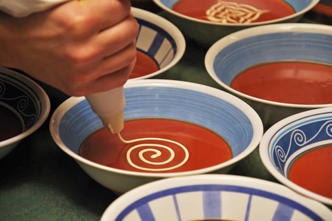 Busy cooks garnish bowls of tomato soup with fresh cream