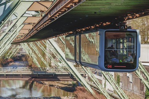 A suspension railway crosses a river in a city, surrounded by architectural metal structures in