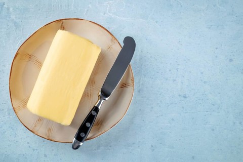 A block of butter with a knife on a plate, overhead flat lay shot on a light slate background, with