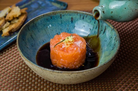 Man turning soy sauce into salmon tartare deliciousness in a beautiful decorated plate