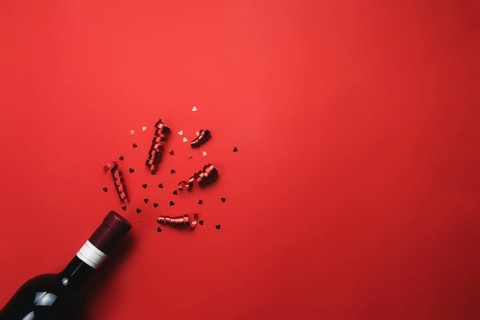 Valentine with bottle of wine, heart glitter and ribbon on red background.