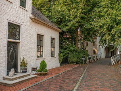 Plants and winding paths along a quiet lane with whitewashed buildings and a wooden bridge, dornum,