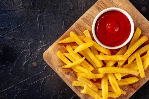 French fries, potato snack with ketchup, fast food on a black stone background, shot from the top