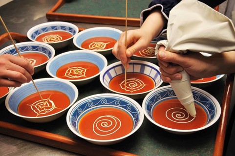 Busy cooks garnish bowls of tomato soup with fresh cream