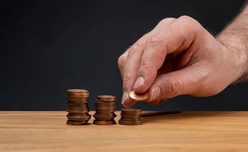 A hand stacking coins on a wooden table against a dark background