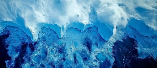 Aerial view of ice cliff meeting the ocean with turbulent waves crashing below, AI generated