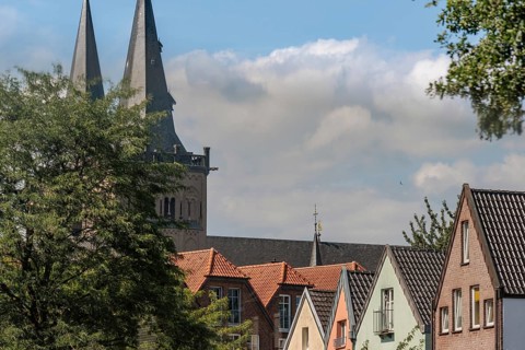 Church tower rises above colourful roof gables of houses under a cloudy sky, Xanten, Lower Rhine,