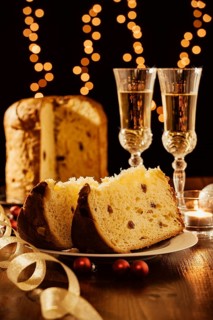 Sliced italian panettone, sparkling wine and decorations with Christmas lights on background