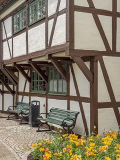 Half-timbered house with white walls and brown wooden beams, planted flower bed and green wooden