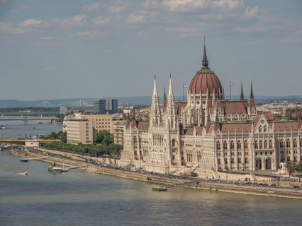 Large historic building on the riverbank with ships on the water and slightly cloudy sky, budapest,