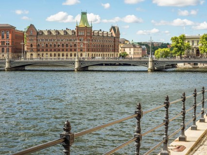 Riverside with a wrought iron railing, a bridge and historic buildings under a sunny sky,