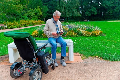 Man sits on a Smart Bensh and charges his Ipad, modern technology, bench with solar panel and