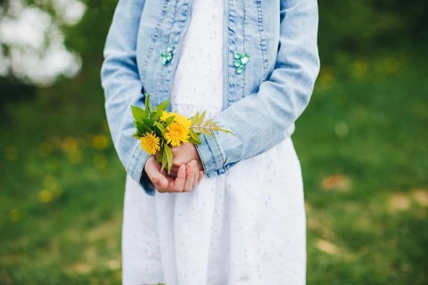 Small girl is holding yellow chamomile flowers.