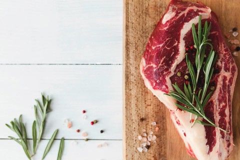 Raw ribeye steak on board, pepper, rosemary and pink Himalayan salt.