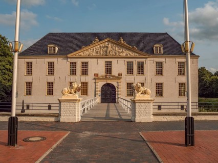 Elegant historic manor house with lion statues and flagpoles against a blue sky, dornum, east