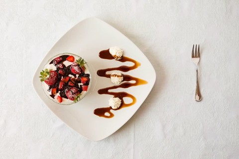 Dessert with strawberries and yogurt in a bowl over a square plate with decorations and cream seen