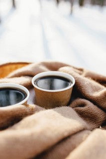 Two cups of coffee on a scarf in the snowy forest.