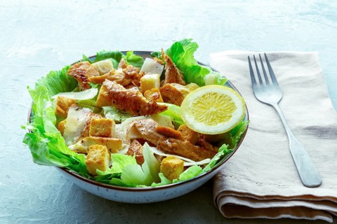 Caesar salad with chicken breast, lettuce, croutons, and a lemon, on a slate background, with a