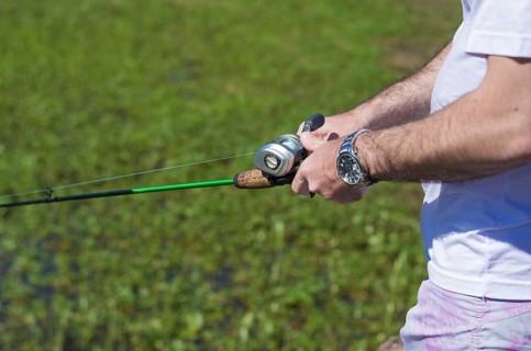 Young man fishing in pond, lake, closeup of fishing rod and reel