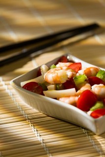 Shrimp salad with squid tomatoes celery inside a white bowl on a bamboo tablecloth and chopsticks
