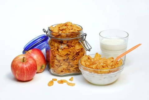 Glass jar and glass bowl with cornflakes, apples, glass with milk, spoon, preserving jar, bowl