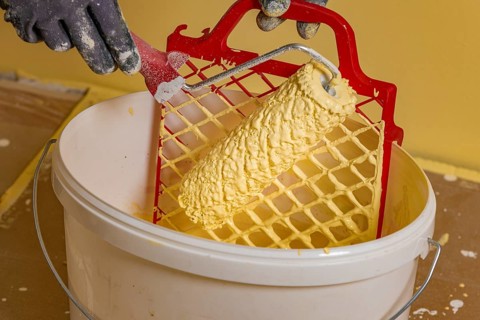 Paint roller on scraper grid in bucket with wall paint, painting work