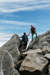Male and female climbers high-fiving at the top of the mountain. Mixed rock climbing team
