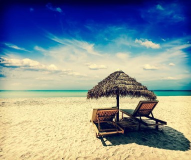 Vintage retro effect filtered hipster style image of two beach lounge chairs under tent on beach.
