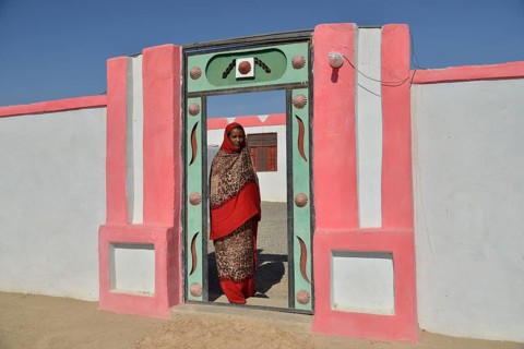 Nubian woman in typical bright dress, in front of her house, in the village of Umogaal in Dongola,