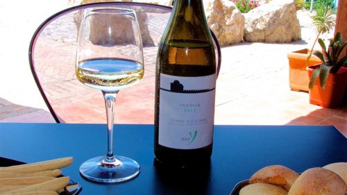 A glass of white wine with the accompanying bottle and snacks on an outdoor table, Sicilian wine,