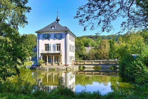 Small cultural heritage baroque castle building called Trappenseeschloss in middle of lake in