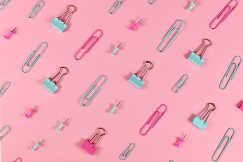 Stationery items like paper clips and drawing pins arranged on pink background