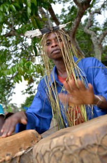 Musician with a headdress made of bast and a feather, playing drums, Nkala, Bandundu Province,