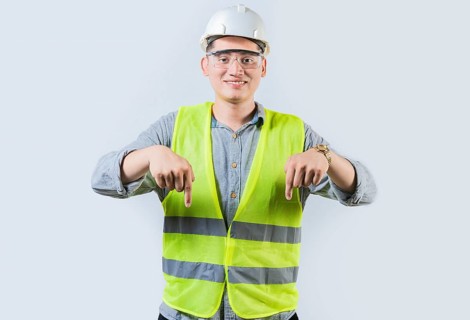 Smiling engineer pointing advertising down isolated. Smiling friendly engineer pointing down