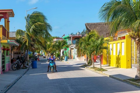 Palm trees motorcycles colourful buildings on quiet village road, Celestun, Yucatan, Mexico,
