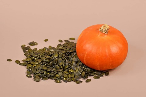 Pumpkin seeds next to whole 'Red Kuri Hokkaido' squash