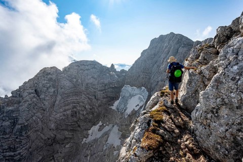 Mountaineer on a rocky narrow mountain path, view of rock faces with blue ice glacier and summit of