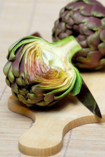 Artichoke (Cynara scolymus Cynara cardunculus) on cutting board with knife (Cynara scolymus, Cynara